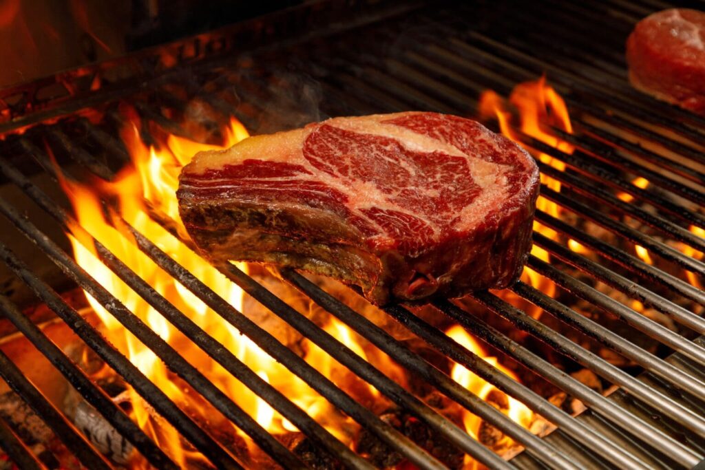 Thick dry-aged bone-in rib steak over open flames at FIRE Steakhouse & Bar